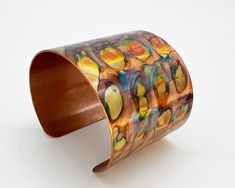 a close up of a metal bracelet on a white surface with an orange and yellow design