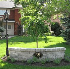 a brick wall in front of a house with a lamp post and tree on the corner