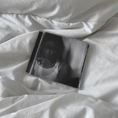 a cd sitting on top of a bed covered in white sheets and blankets with a person's face