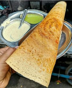 a person holding a pita with dips and sauces on the other side