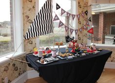 a black table topped with lots of food next to a flag and window sill