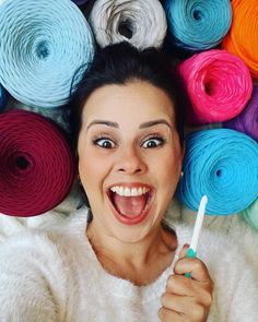 a woman holding a toothbrush in front of many skeins of colored yarn