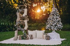 an outdoor setting with christmas trees and presents on the grass, in front of a sunset