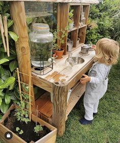 a little boy standing next to a wooden planter filled with plants and water in it