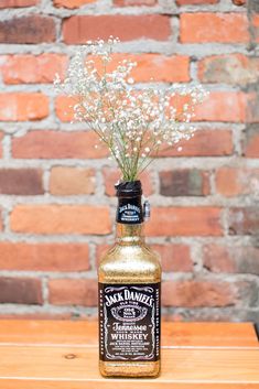 a bottle filled with flowers sitting on top of a wooden table next to a brick wall