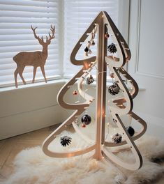 a wooden christmas tree with ornaments on it in front of a window and white blinds