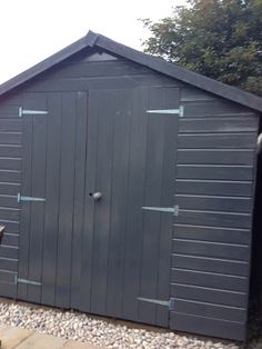 a black shed sitting on the side of a road next to a bench and trees