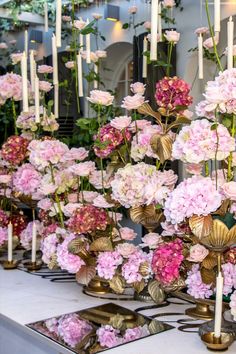 a table topped with lots of pink flowers and gold vases filled with white candles