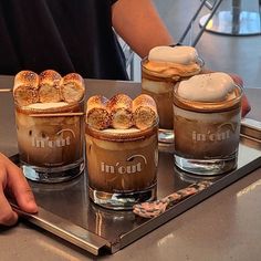 there are three desserts in glasses on the table with someone's hand next to them