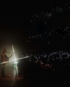 a woman standing in front of a microphone on top of a stage with lights behind her