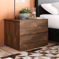 a nightstand with a potted plant on it next to a bed