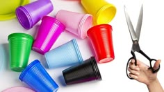 there are many different colored cups and scissors in this photo, with one person holding the scissors