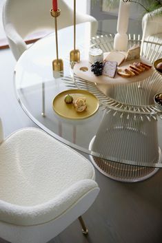 a glass table topped with white chairs and plates