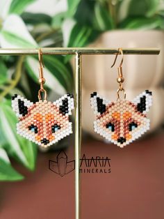 a pair of earrings with an orange and black fox design on them, hanging from a metal stand