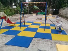 an empty playground with blue and yellow tiles on the ground, swings and slides in the background