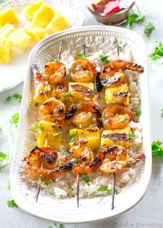 grilled shrimp and pineapple skewers on rice in a white serving dish