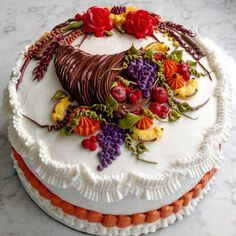 a cake decorated with fruit and flowers on top of a marble tablecloth covered in white frosting