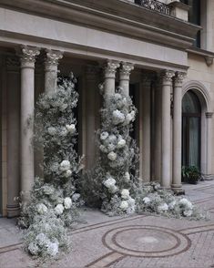 some white flowers are on the ground in front of an old building with columns and arches