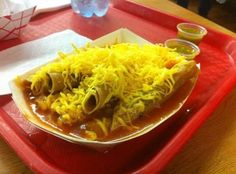 a red tray topped with a chili cheese enchilada covered in condiments