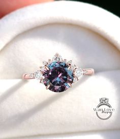 a pink and blue diamond ring sitting on top of a white cloth