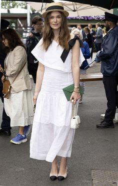 a woman in white dress and hat standing under an umbrella