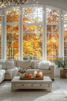 a living room filled with furniture and windows covered in fall colored trees behind the couch