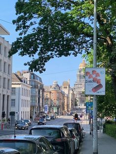 cars parked on the side of a street next to tall buildings and trees in front of them