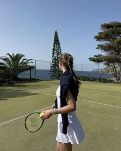 a woman holding a tennis racquet on top of a tennis court with the ocean in the background