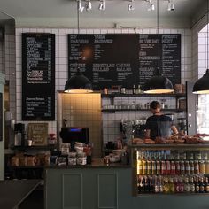 a person standing behind a counter in a restaurant with menus on the wall and lights hanging from the ceiling