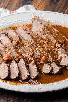 a white plate topped with meat covered in gravy on top of a wooden table