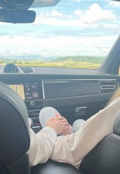 a woman sitting in the driver's seat of a car with her feet on the steering wheel