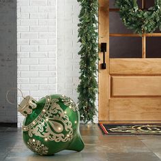 a green vase sitting on the floor next to a door with greenery around it