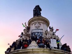 a group of people standing on top of a statue with flags flying in the air