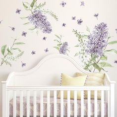 a white crib in front of a wall with purple flowers and butterflies on it