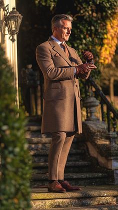 a man in a brown suit and tie standing on steps with his hands clasped to his chest