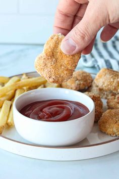 a person dipping something into a bowl of ketchup on a plate with french fries