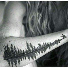 a person with a tattoo on their arm that has trees and birds flying over them