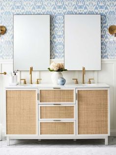 two mirrors are above the double sink vanity in this white and gold bathroom with blue wallpaper