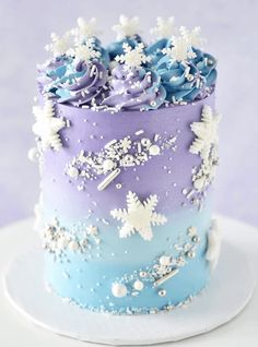 there is a blue and purple cake with white flowers on the top, and snow flakes all over it