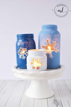 three mason jars with candles in them sitting on a cake plate, one blue and the other white