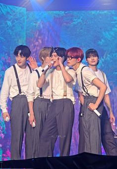 group of young men standing on stage with one holding his head in the air and two wearing suspenders