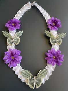 a necklace made out of dollar bills and purple flowers on a black surface with butterflies