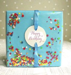 a blue gift box with confetti on it and a happy birthday tag attached