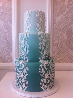 a three tiered blue and white cake with intricate designs on the top, sitting on a table