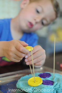 a young boy is playing with some buttons on a blue and green cake that he made