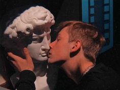 a young man kissing a statue of two heads in front of a building with the words meanland written on it