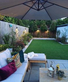 an outdoor patio with white couches and green grass in the back yard, next to a wooden table