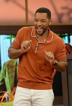 a man in an orange shirt and white pants with his fist up while standing next to a tv