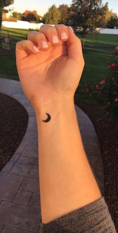 a woman's arm with a small black crescent tattoo on the left side of her wrist