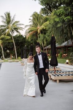 a bride and groom are walking together in front of an outdoor area with umbrellas